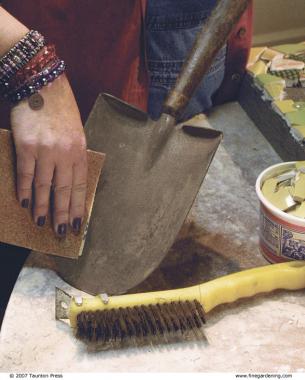 hand using sandpaper to remove rust from a shovel; brush nearby