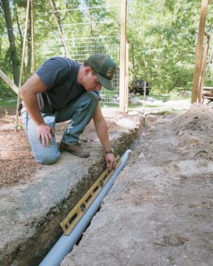 Laying a length of rigid pipe in the trench before measuring with a 4-foot level